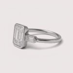 Front view of three-stone engagement ring with emerald cut center diamond and baguette sides in white gold