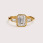 Front view of three-stone engagement ring with emerald cut center diamond and baguette sides in white gold