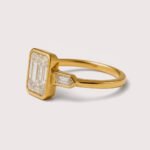 Front view of three-stone engagement ring with emerald cut center diamond and baguette sides in white gold
