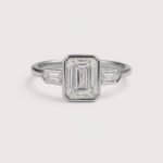 Front view of three-stone engagement ring with emerald cut center diamond and baguette sides in white gold