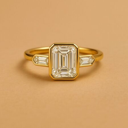 Front view of three-stone engagement ring with emerald cut center diamond and baguette sides in yellow gold