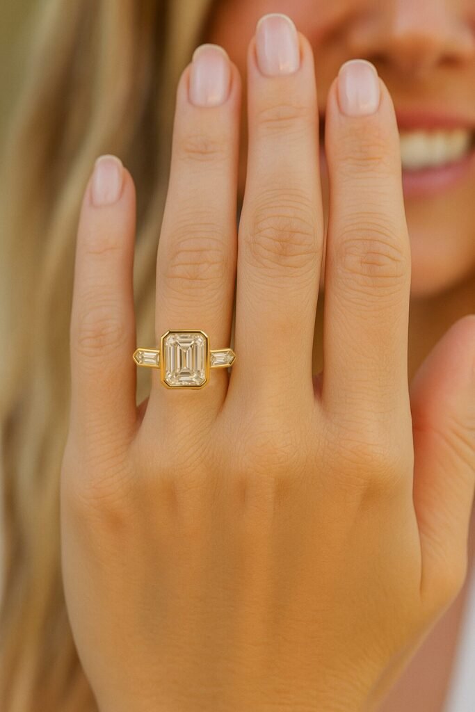 UN1012 (5) Emerald cut three-stone diamond engagement ring in yellow gold on a woman's hand