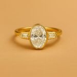 Side profile of oval cut diamond ring with tapered baguette diamonds in yellow gold band