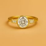 Front view of yellow gold three-stone engagement ring featuring round brilliant cut diamond and tapered baguettes