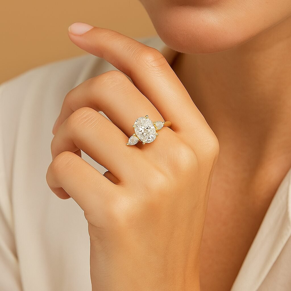 UN1021 (2) Woman wearing an oval diamond three-stone engagement ring with yellow gold band, elegant hand pose.