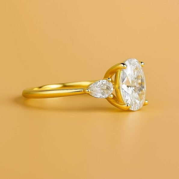 Close-up side angle of an oval diamond ring with pear side stones in yellow gold, minimalist straight shank.