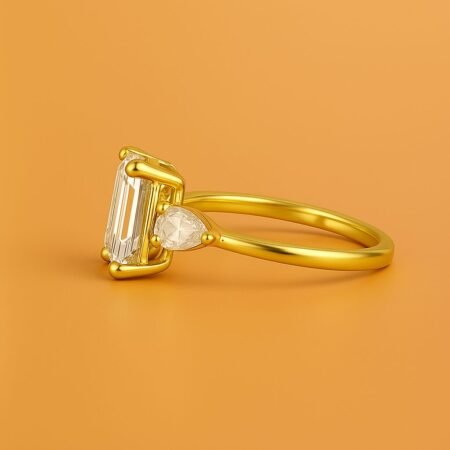 Side view of emerald cut diamond ring with pear-shaped side stones set in yellow gold, modern straight shank.
