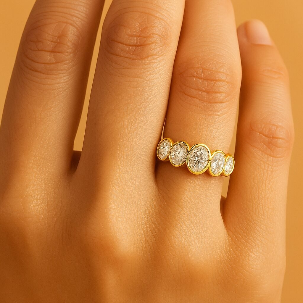 Woman wearing a five-stone bezel set round diamond ring in yellow gold, close-up hand view.