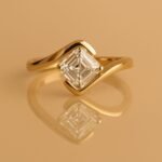Elegant Asscher cut lab-grown diamond ring in yellow gold with bypass setting, reflecting on a glossy background