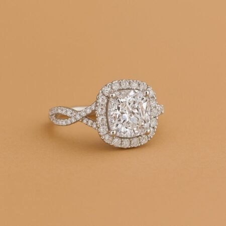 Cushion cut diamond halo engagement ring with pavé twisted band in white gold on beige background.
